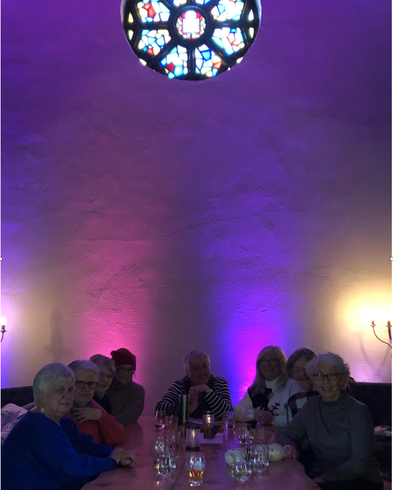 Eight women sit at a table in purple lighting underneath the round rose window of the Church Brewery restaurant.